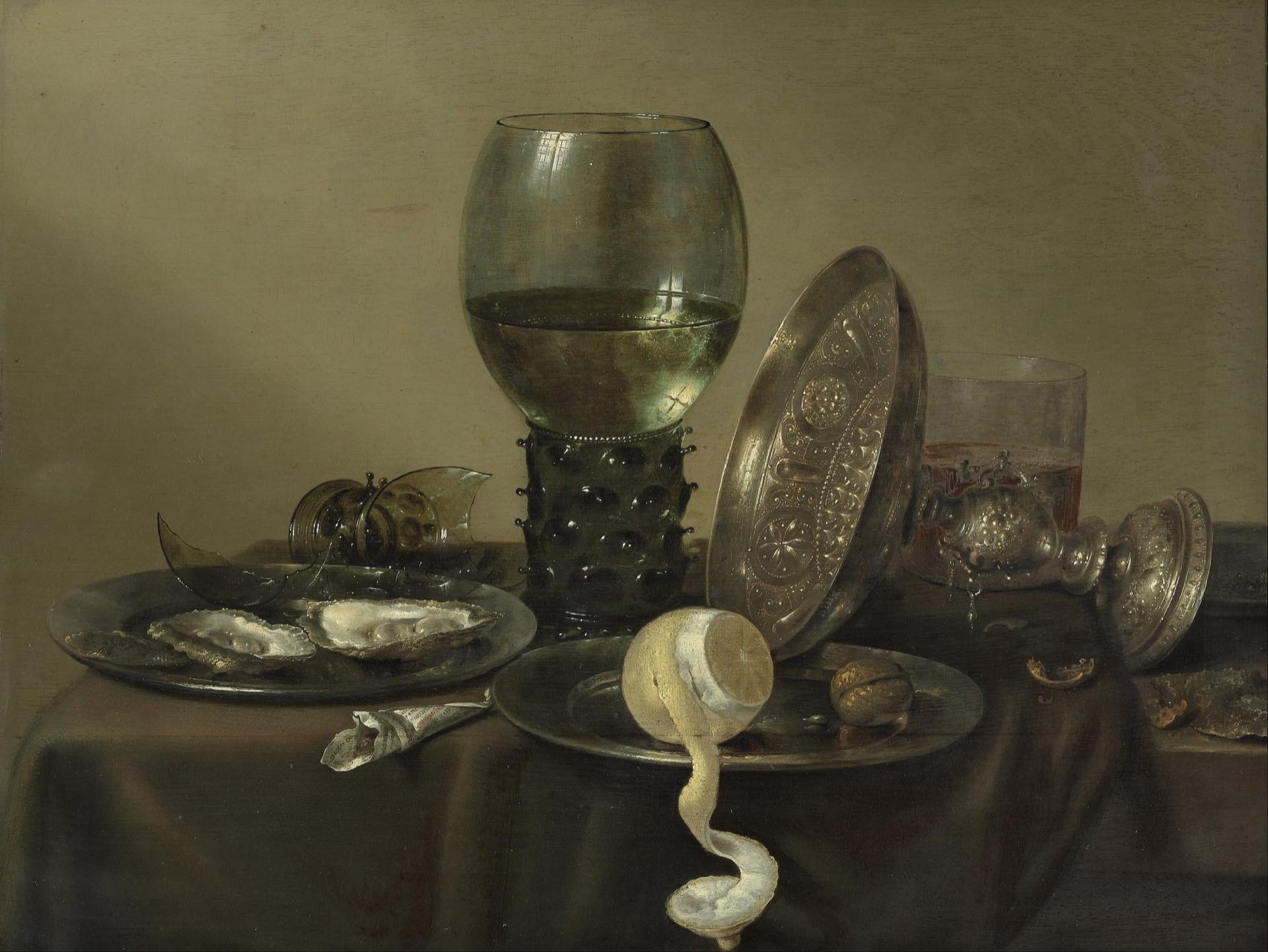 A still life of oysters, a lemon, a silver bowl and a glass on a laid table